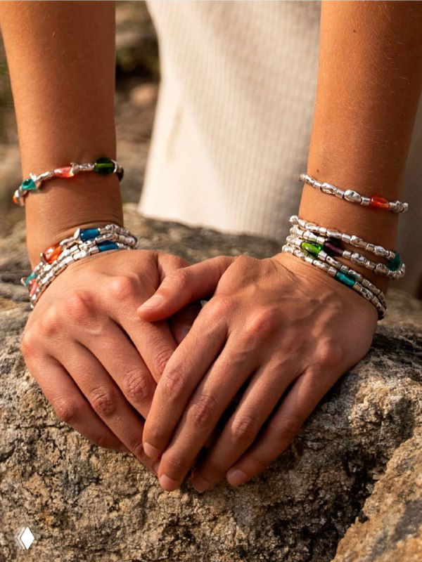 Руки модели украшены разноцветными браслетами Liquid Ciclon, видны стеклянные бусины, металлические соединения и застёжки.