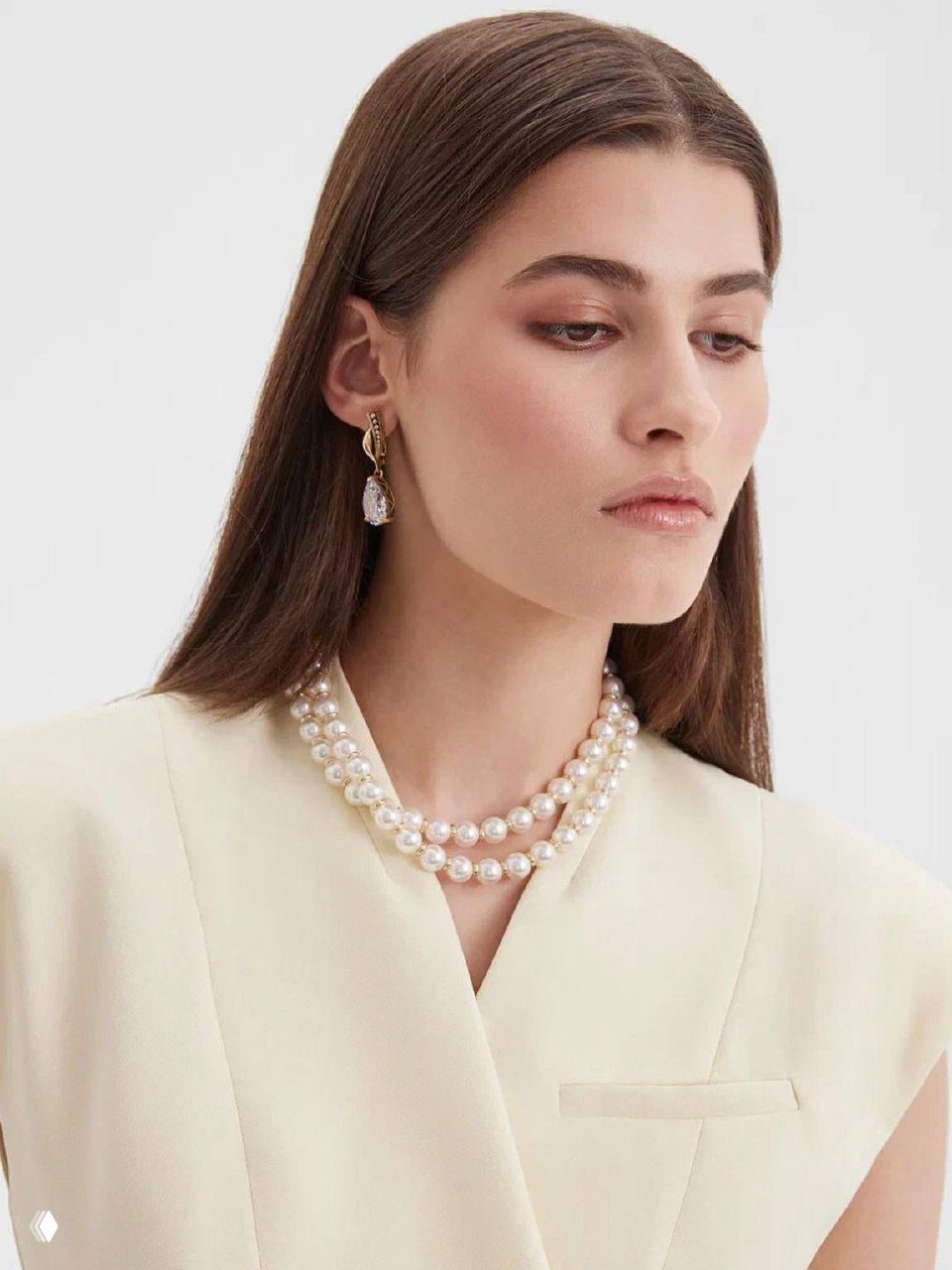 Модель в кремовом жакете демонстрирует двойную нить белого жемчуга на шее и элегантные золотые серьги, фотосъёмка для каталога магазина.