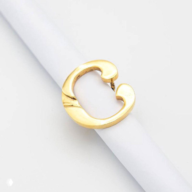 Золотистое кольцо в форме буквы «C» на белом держателе, студийный крупный план с акцентом на форму, глянцевую поверхность и отделку изделия.