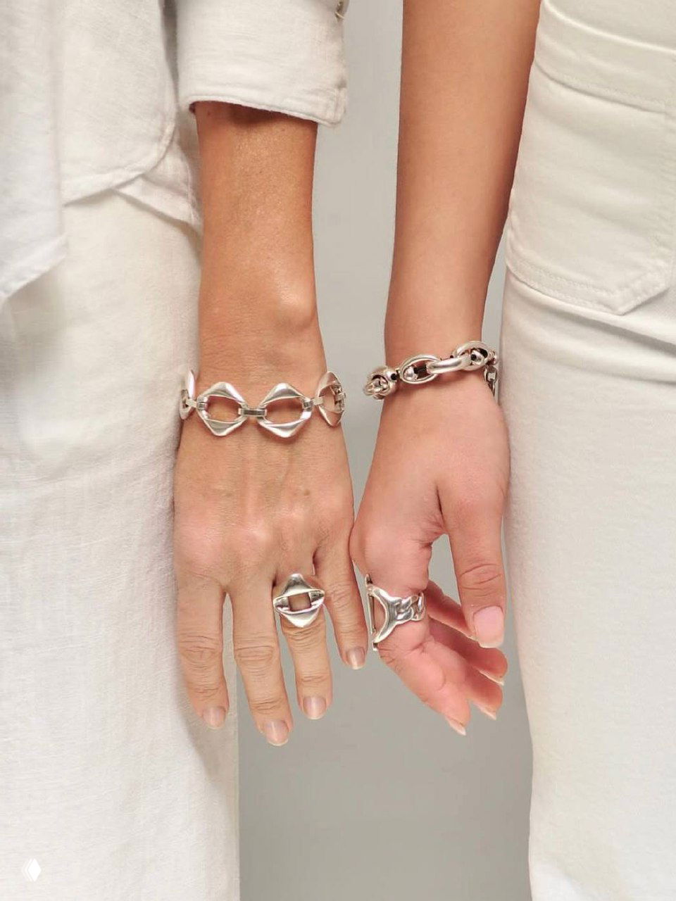 Крупный план двух женских рук и запястий в светлой одежде, украшенных серебряными браслетами и кольцами в лаконичном стиле бренда CICLON на нейтральном фоне.