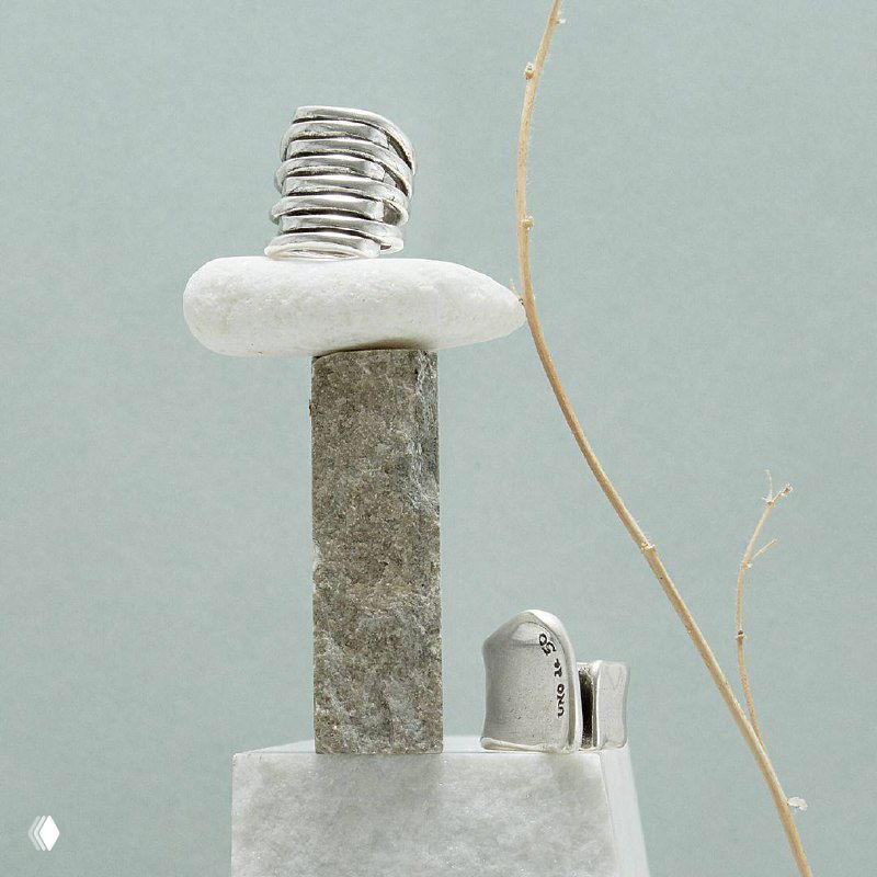 Серебристые украшения UNOde50 выставлены на минималистичной подставке — акцент на форме, фактуре и материале изделий бренда.