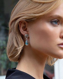 Крупный план профиля модели в серьгах из коллекции Ciclon LIQUID: серебристая фурнитура и бирюзовые муранские стеклянные подвески на нейтральном фоне.