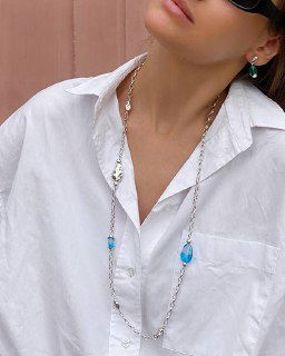 Модель в длинной цепочке-ожерелье Ciclon LIQUID с бирюзовыми вставками на белой рубашке: минималистичный стиль и акцент на украшении.