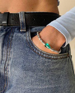 Крупный план браслета Ciclon LIQUID в кармане джинсов: зеленовато-бирюзовые муранские элементы и серебристая цепочка на повседневной одежде.