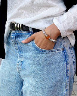 Запястье в браслете LIQUID на фоне светлых джинсов: сочетание металлической текстуры и тёплых янтарных стеклянных вставок, подчёркнутое естественным светом.