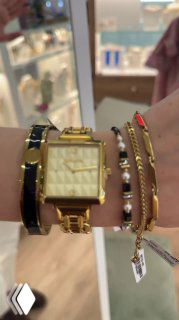 Запястье с золотыми часами и несколькими браслетами, крупный кадр из витрины магазина — сочетание разных текстур и дизайнов аксессуаров.