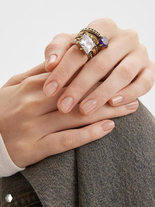 Руки модели с массивными кольцами Fiore di Firenze: крупный прозрачный камень и фиолетовая вставка на соседнем колце, нюдовый маникюр.