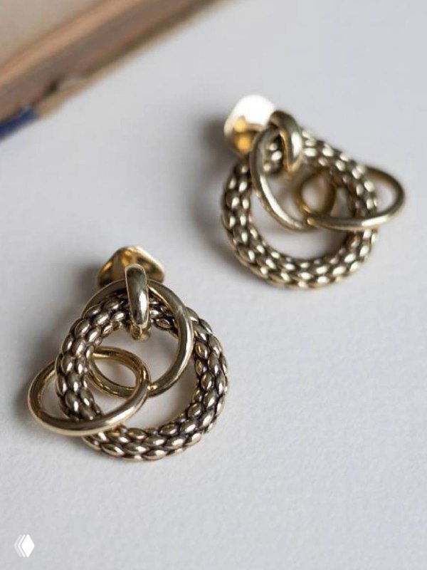 Парные серьги в плоской композиции на столе: скрученные детали и текстура металла Fiore di Firenze, естественное освещение подчёркивает форму.