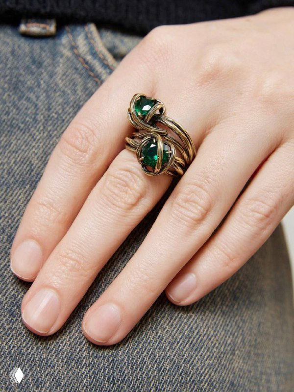 Крупный кадр руки с кольцом Fiore di Firenze с зелёными камнями; латунное покрытие и филигранный винтажный узор на тканевом фоне.