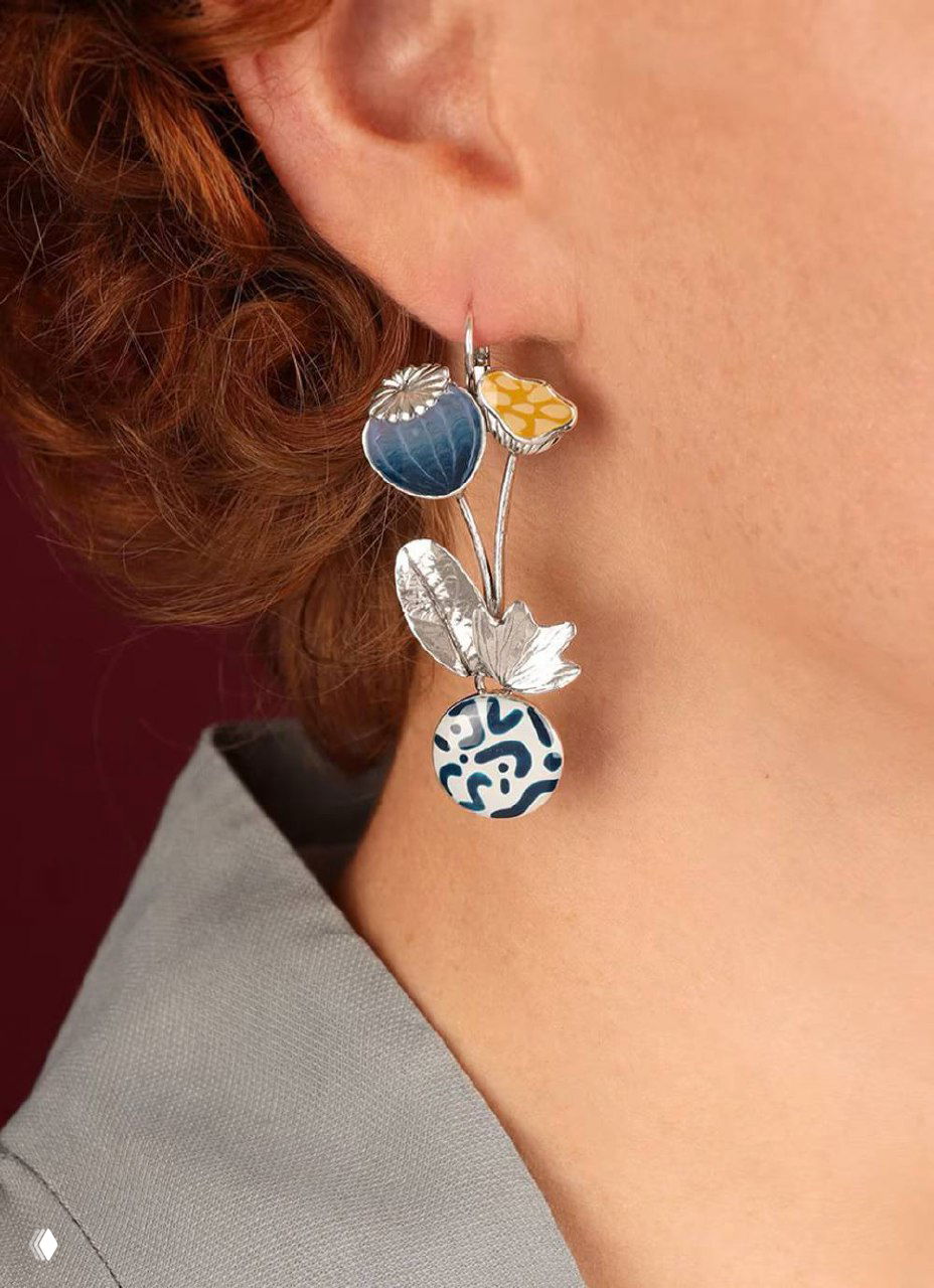 Крупный план серьги TARATATA с цветочными эмалевыми подвесками и серебристой основой на ухе модели, демонстрирующий посадку и фактуру украшения.