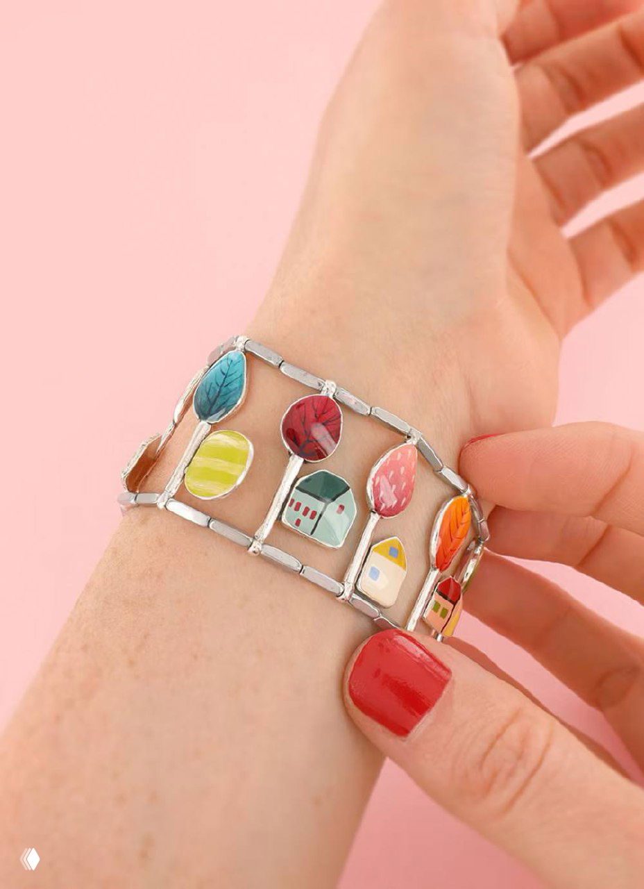 Широкий эмалевый браслет TARATATA с разноцветными подвесками и домиками, надет на запястье — подчёркнутый ручной декор и фактура эмали.