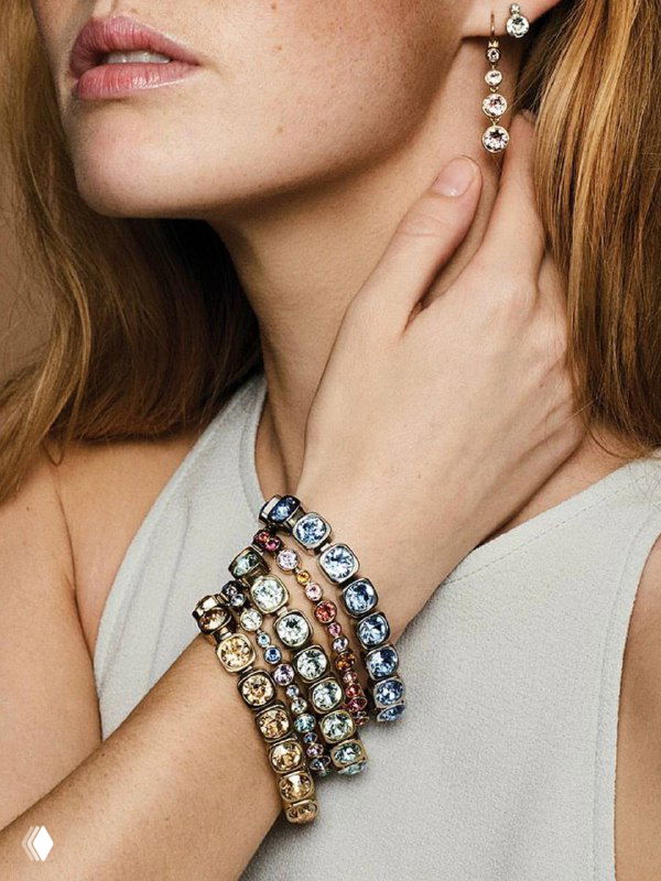 Крупный план запястья модели с несколькими кристальными браслетами Dyrberg Kern и изящными серьгами на нейтральном фоне.