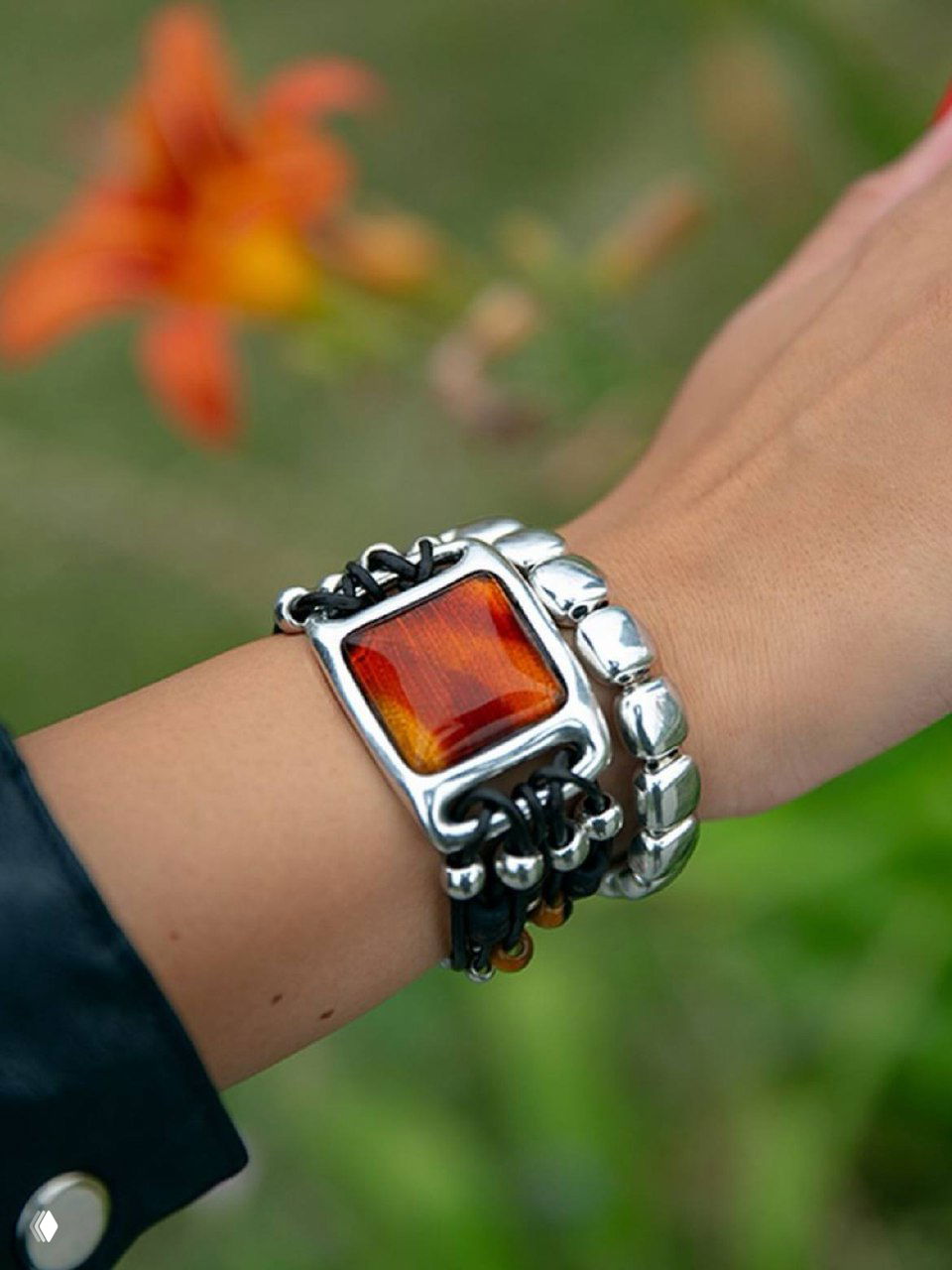 Фрагмент запястья с браслетом KUBIK Ciclon: янтарный коричневый камень, сочетание кожаных шнуров и серебристых звеньев на естественном фоне.