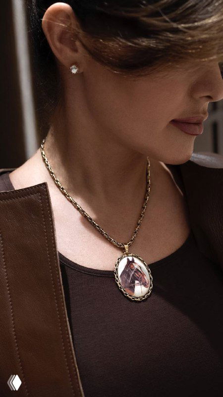 Крупный кадр: модель в полупрофиле носит золотую цепочку с овальным медальоном и маленькой серьгой, показано, как украшение смотрится в образе.