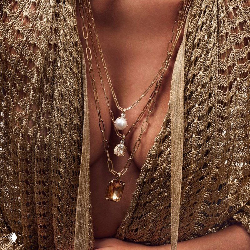 Модель в нескольких слоях золотых цепочек с подвесками и жемчужинами Dyrberg Kern; стилизованная съёмка подчёркивает сочетание текстур и слоёв украшений.