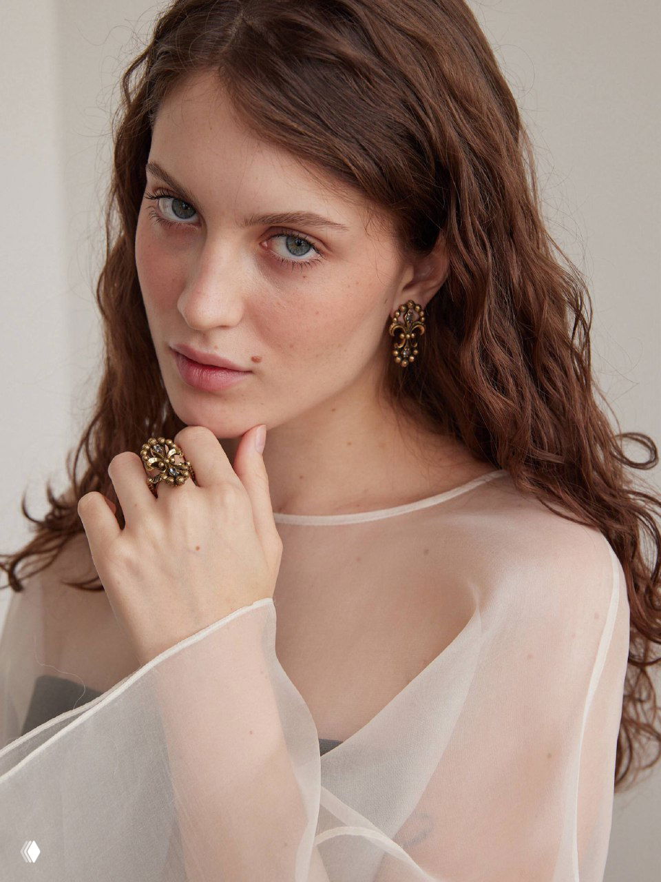 Портрет модели в прозрачной блузе, демонстрирующей серьги и кольцо из коллекции IRIS ARALDICO NOVA бренда Fiore di Firenze; золотистая фактура и фиолетовые вставки, винтажная эстетика.