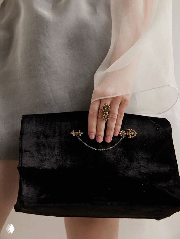 Рука модели с кольцом и бархатной сумкой: композиция демонстрирует сочетание аксессуаров IRIS ARALDICO NOVA с вечерним образом и фактурами тканей на нейтральном фоне.