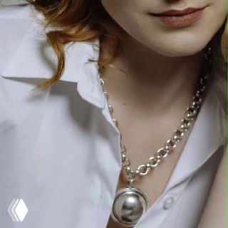 Женская шея в белой рубашке, на ней массивное серебристое ожерелье Ciclon — пример стилизации украшения на модели.