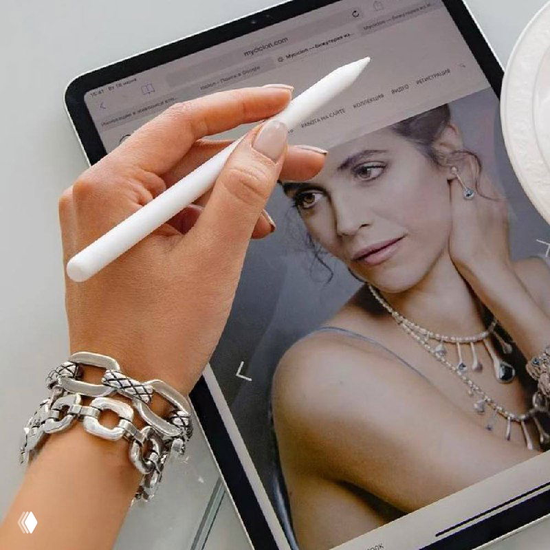 Руки с планшетом и стилусом рядом с рекламным изображением украшений, стилизованная фотография — сочетание бижутерии и lifestyle-контекста.