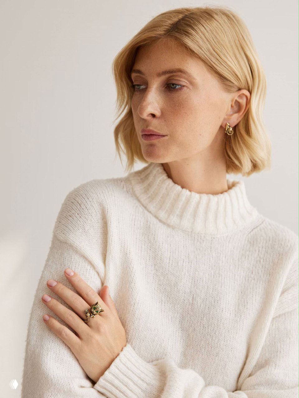 Модель в белом свитере демонстрирует золотистые серьги и кольцо из коллекции Gatto e Topo от Fiore di Firenze, крупный план.