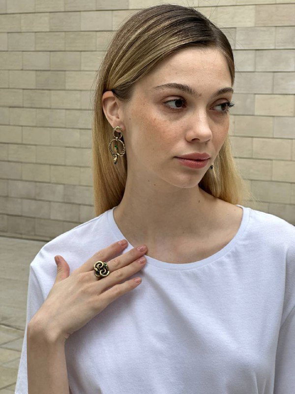 Модель в анфас демонстрирует комплект украшений: серьги и кольцо в стиле змеи, образ в естественном светлом интерьере магазина