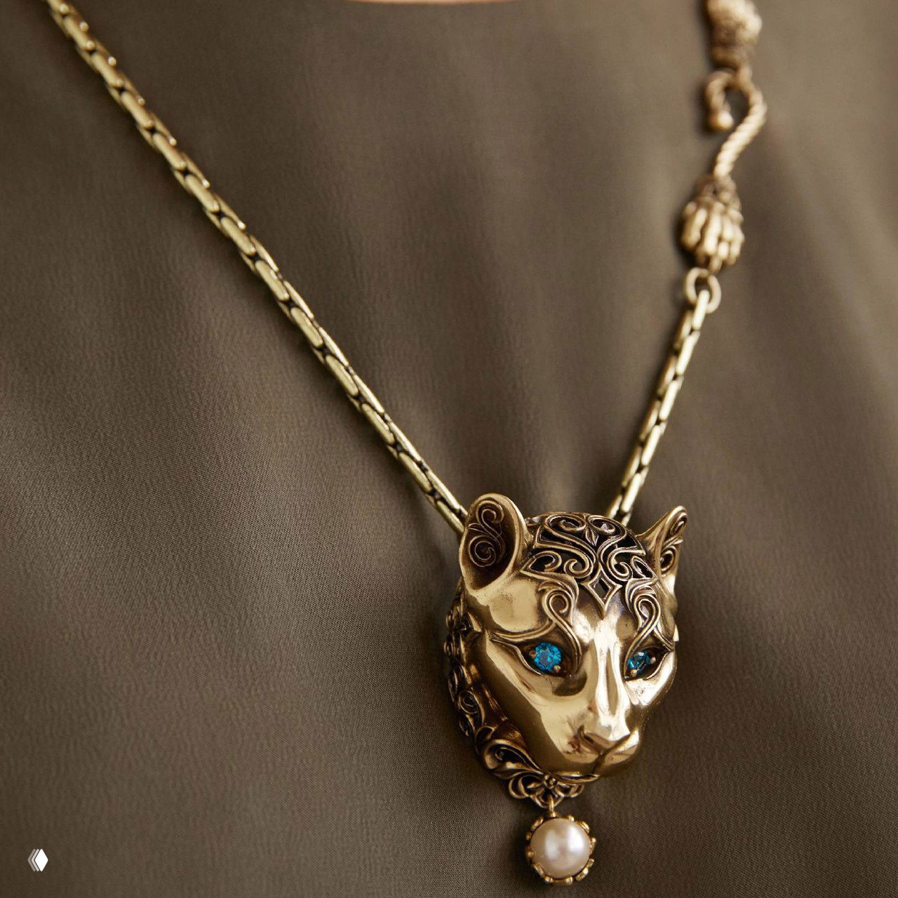 Крупный план кулона Fiore di Firenze в виде головы пумы: золотистый металл, рисунок и инкрустация голубыми кристаллами в глазах, тонкая цепочка.