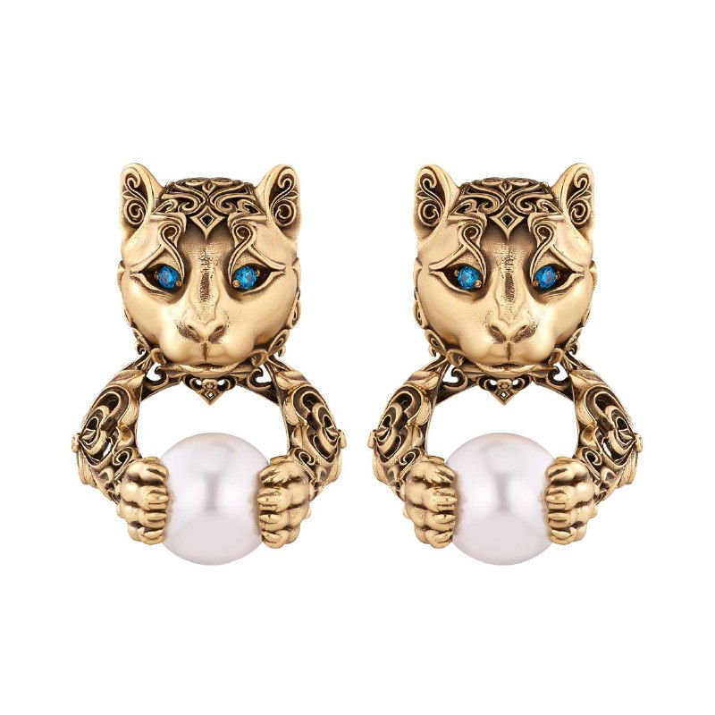 Пара серьг с изображением головы пумы и держанием жемчужины в лапах: золотистая отделка и контрастные светлые жемчужины на белом фоне.