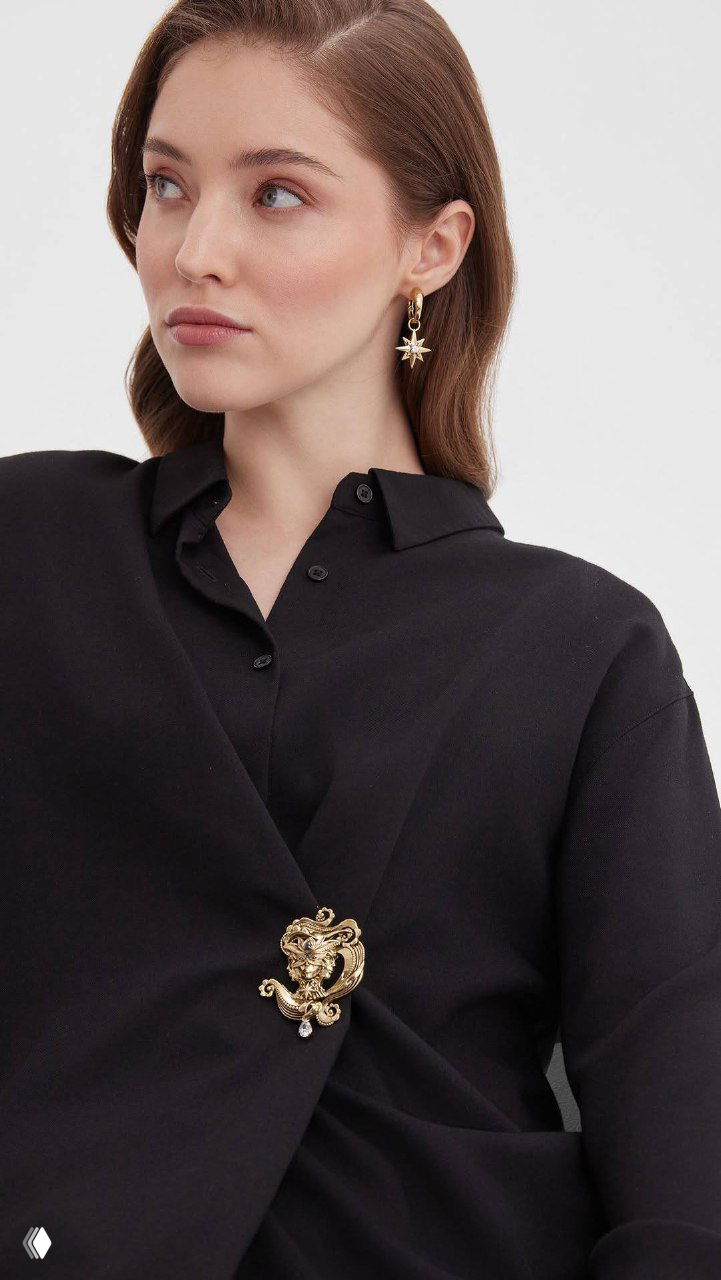 Модель в чёрной блузе демонстрирует украшения из коллекции VELOCITA Del VENTO: брошь и серьга в золотистом оттенке, стилизованные под ветвь и звезду.