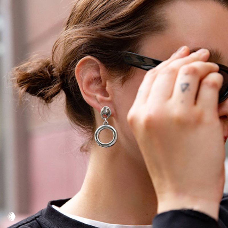 Крупный план серьги из коллекции Aurea от Ciclon: серебристые круглые подвески на ухе модели, детальная текстура металла и городской фон