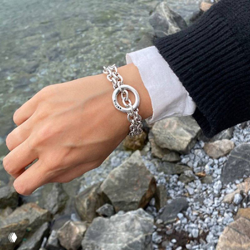 Браслет Aurea от Ciclon на запястье модели рядом с морским побережьем: серебристые звенья и массивная текстура, стильная уличная съёмка