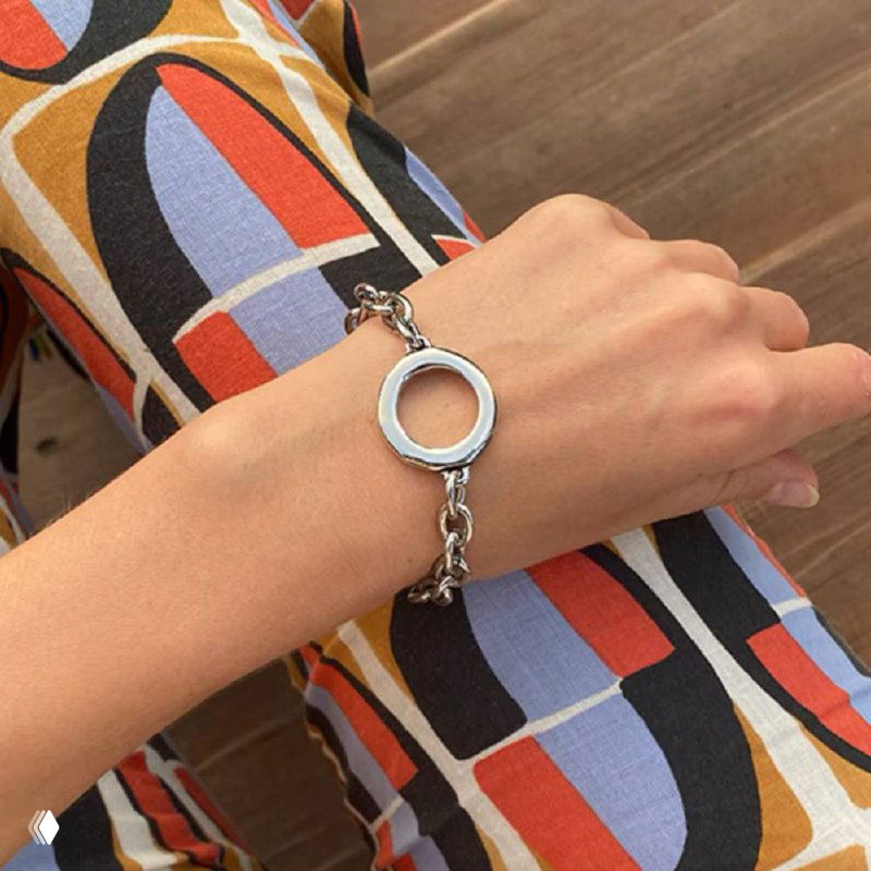 Браслет Aurea на запястье модели в интерьере: тонкая цепочка и круглый декоративный элемент, демонстрация посадки украшения на руке