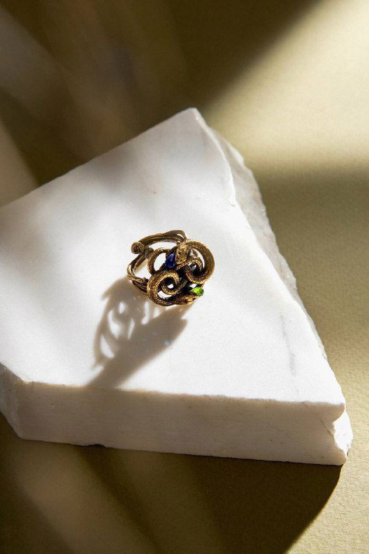 Кольцо в виде закрученной змеи на мраморной плитке под направленным светом, демонстрируется дизайн и игра бликов на металле