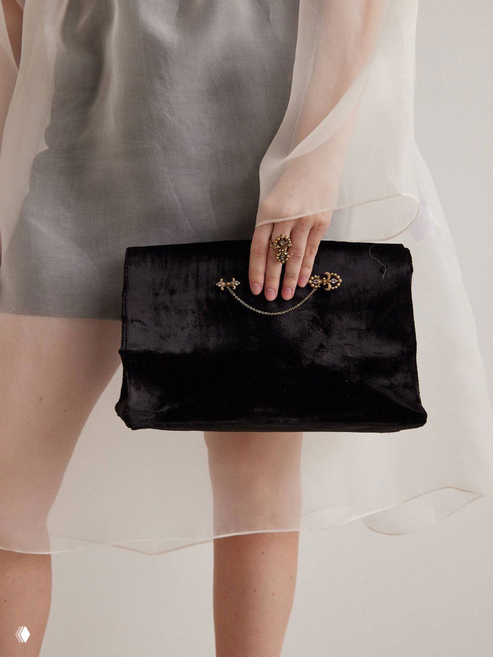 Женская рука держит бархатный клатч с декоративной брошью у ручки — идея закрепления броши на сумке для акцента