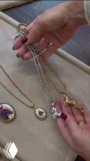 Крупный план: руки держат несколько золотых и серебряных цепочек с подвесками в виде лошади и овальными медальонами, кадр из видео презентации коллекции.