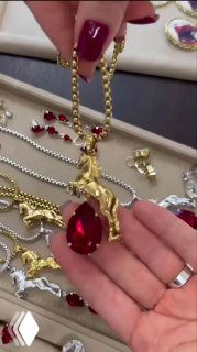 Кадр видео: демонстрация крупного золотого кулона-лошади с большим красным каплевидным кристаллом в руках консультанта, презентация дизайна.