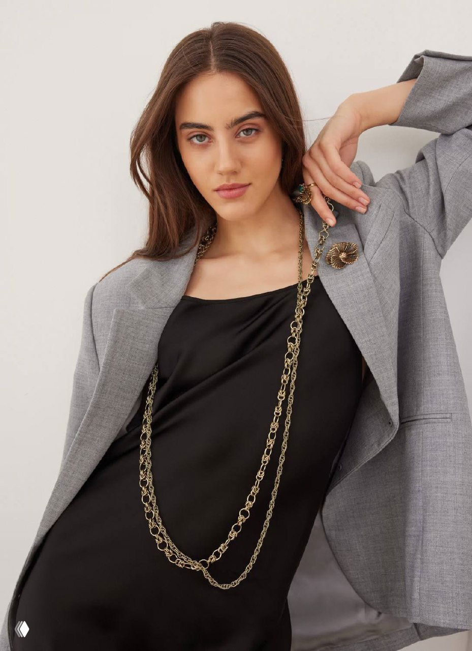 Модель в сером пиджаке и чёрном платье демонстрирует длинную золотую цепь Fiore di Firenze, образ с лёгкой неформальной элегантностью.