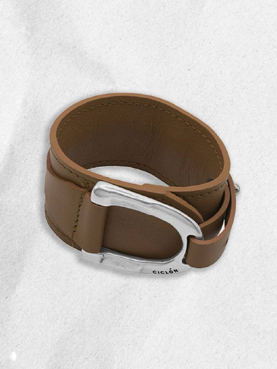 Крупный план коричневого кожаного браслета с широкой серебряной пряжкой и маркировкой, демонстрация текстуры и детали изделия