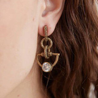 Крупный кадр уха модели, на котором надеты серьги коллекции Cavallo: золото текстурированного металла и декоративный подвес с кристаллом, демонстрация посадки на ухе.