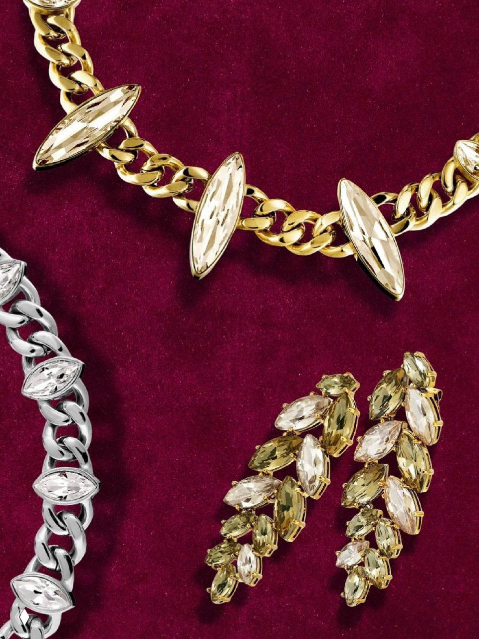 Крупный план украшений DYRBERG KERN на бордовом фоне: золотистая и серебристая цепочки с маркиз-камнями и пара эффектных серёжек.