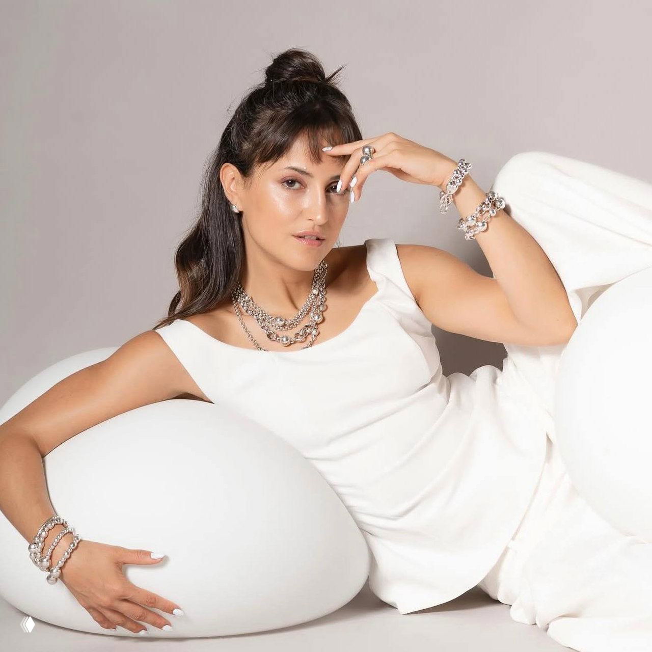 Модель в белом демонстрирует украшения Spheric от Ciclon: цепи, браслеты и кольца на светлом нейтральном фоне.