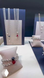 Витрина с подвесками и браслетами коллекции SPHERIC от CICLON: серебристые цепочки и шарики с вставками муранского стекла разных цветов.