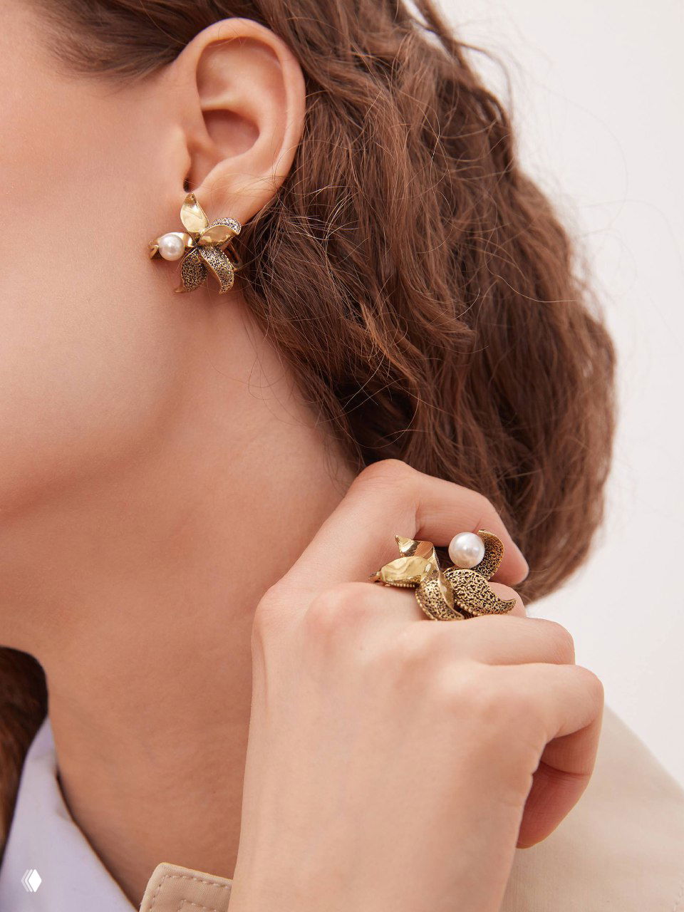 Крупный кадр уха и руки: цветочный дизайн серьги и крупное кольцо Fiore di Firenze с жемчугом и металлизированными деталями.