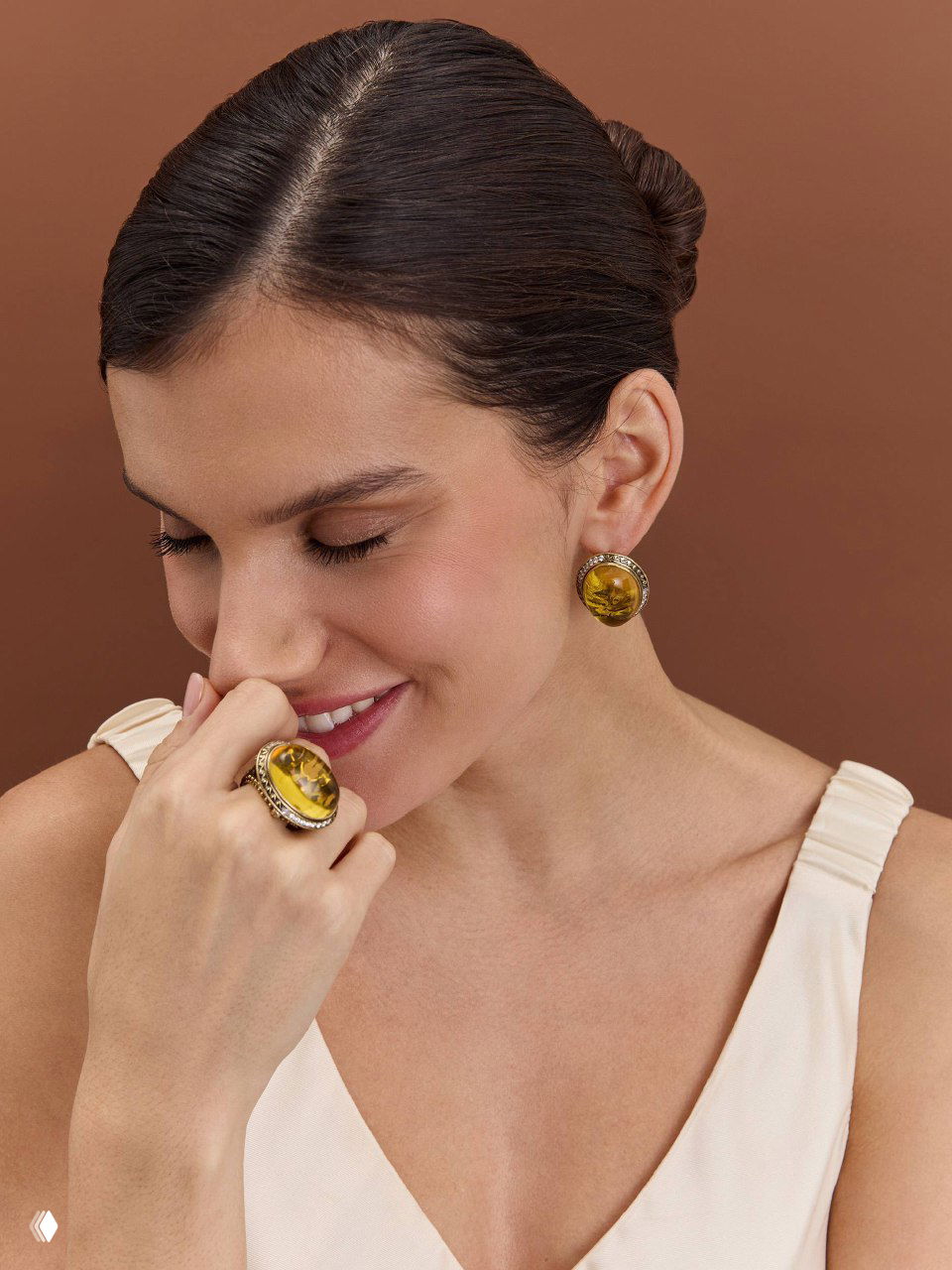 Улыбающаяся модель в пастельном топе показывает серьги и крупное кольцо с янтарным или жёлтым камнем из коллекции Fiore di Firenze.