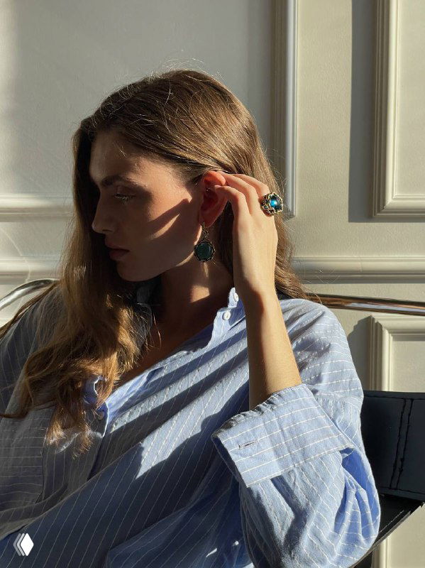 Модель у окна в рассеянном свете демонстрирует темно-зелёные серьги и кольцо Fiore di Firenze — атмосферный снимок с тёплыми тенями.