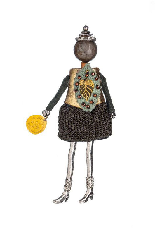 Брошь-кукла MIAMELIE на белом фоне: тёмная головка, украшение на груди в виде декоративного листа и фактурное платье из ткани и металла