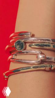 Крупный план нескольких металлических браслетов UNOde50 на женском запястье на красном фоне, рекламный кадр коллекции аксессуаров.