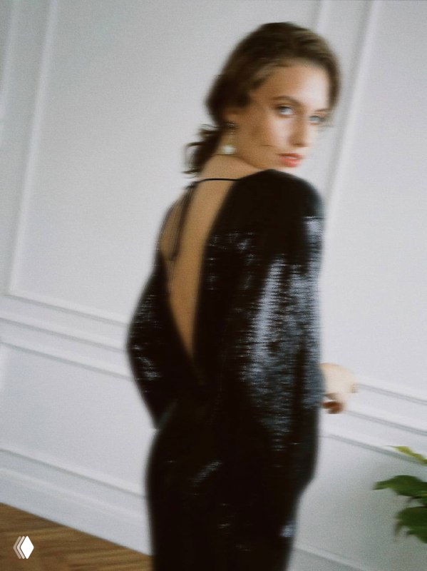 Модель в чёрном блестящем платье позирует в интерьерной съёмке, демонстрируя авторские украшения и праздничный образ для Нового года.