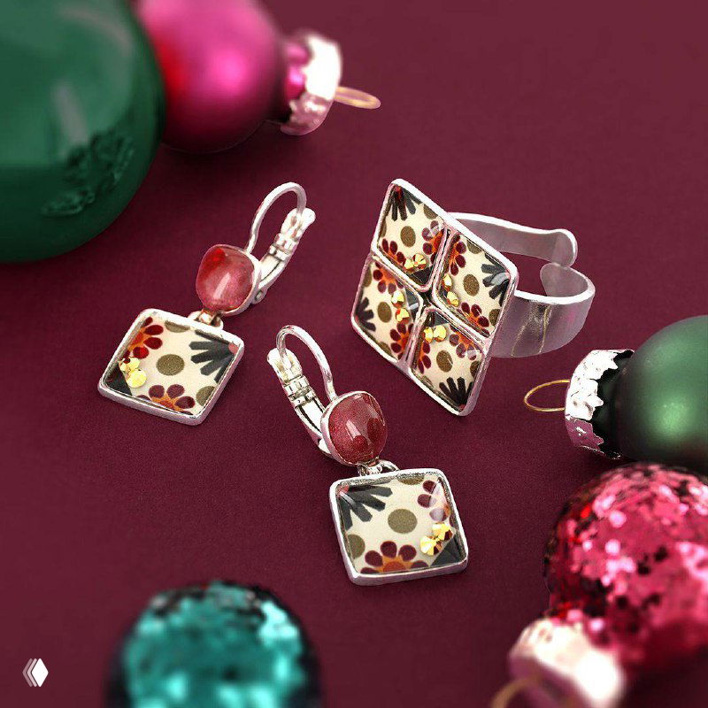 Набор серьги и кольцо с флоральным узором и красными вставками, разложенные на бордовом фоне с новогодними игрушками — аксессуары в винтажном стиле.
