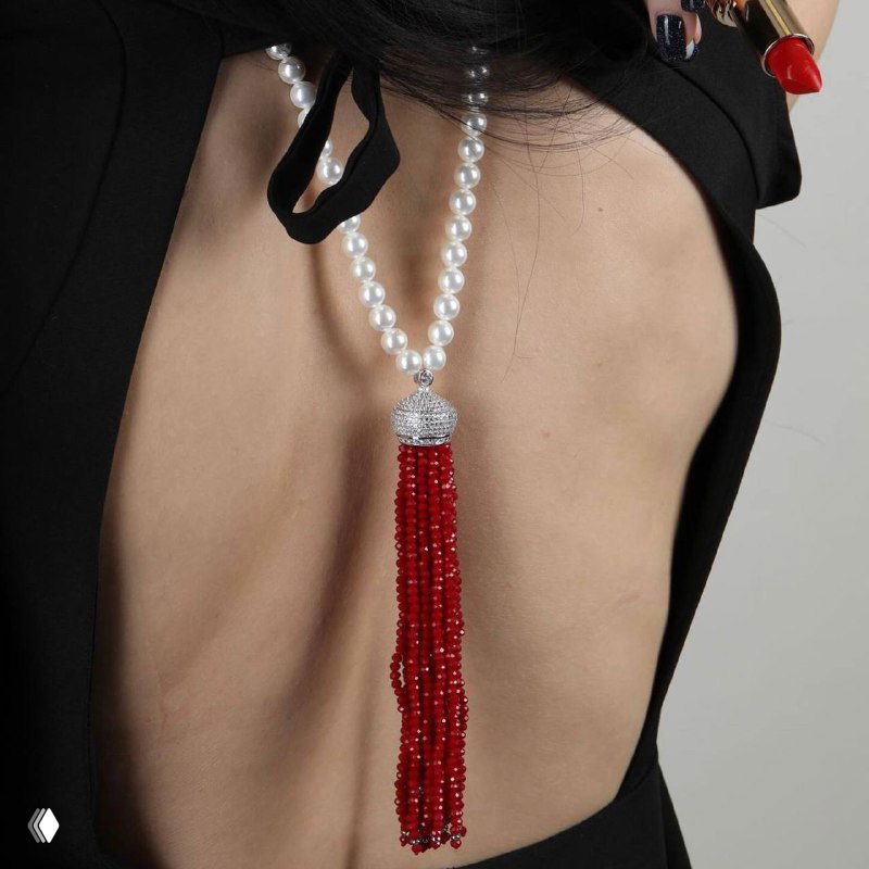 Длинное жемчужное ожерелье с ниспадающей красной кистью на обнажённой спине модели — эффектное вечернее украшение для праздничного образа.