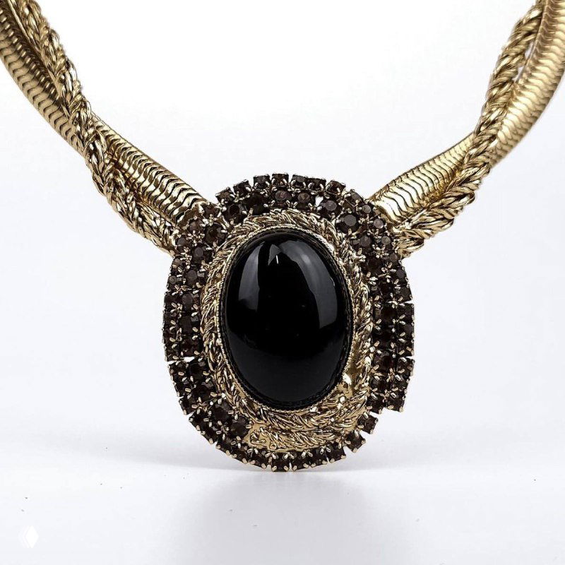 Золочёное ожерелье с крупным чёрным кабошоном в центральной оправе и декоративной текстурой по периметру — элегантный декоративный элемент.
